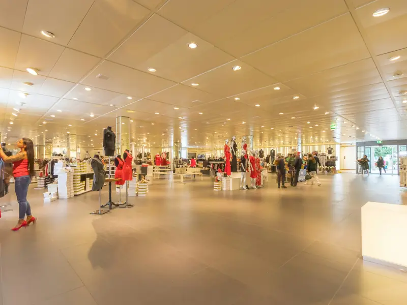 Spacious department store sales floor with clothing displays under bright recessed ceiling lights