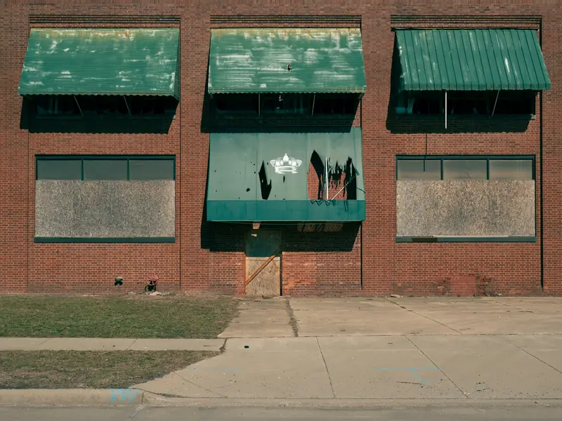 Brick commercial building with plywood boarded windows under weathered green awnings