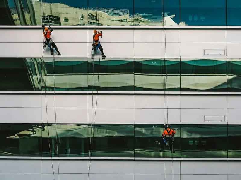 Rope-access crew cleaning the glass windows of a white commercial office building